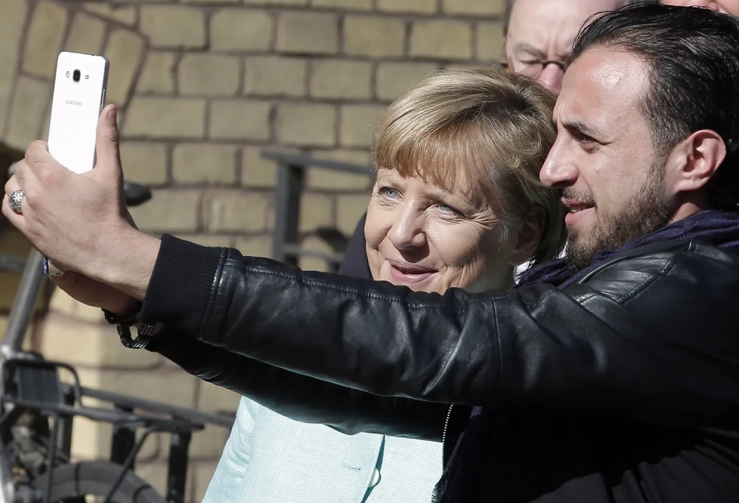 In this Sept. 10, 2015, file photo, refugee Rodin Saouan from Syria takes a picture of himself and German Chancellor Angela Merkel, left, during Merkel's visit at a registration center for migrants and refugees in Berlin, Germany. (AP)
