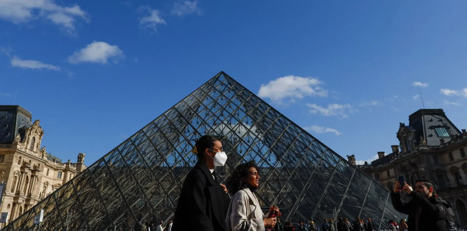 People wearing protective face masks walk near the glass Pyramid of the Louvre museum in Paris, amid the coronavirus disease (COVID-19) outbreak in France, February 19, 2022. (Reuters)