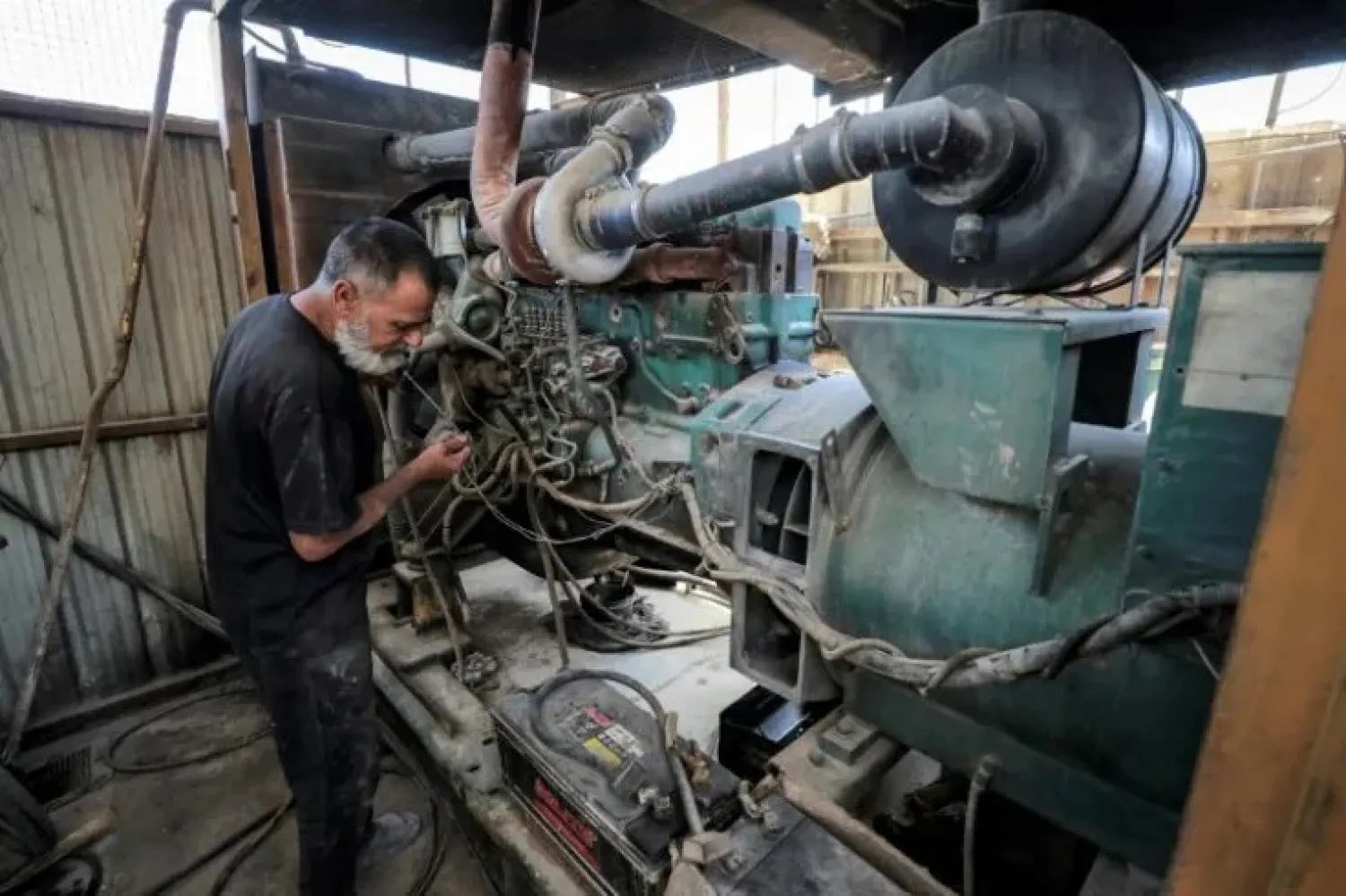 A technician checks the oil on the dipstick of one of the fuel-based electricity generators in a battery in the eastern Sadr City suburb of Iraq's capital Baghdad on September 27, 2022. (Photo by AHMAD AL-RUBAYE / AFP)