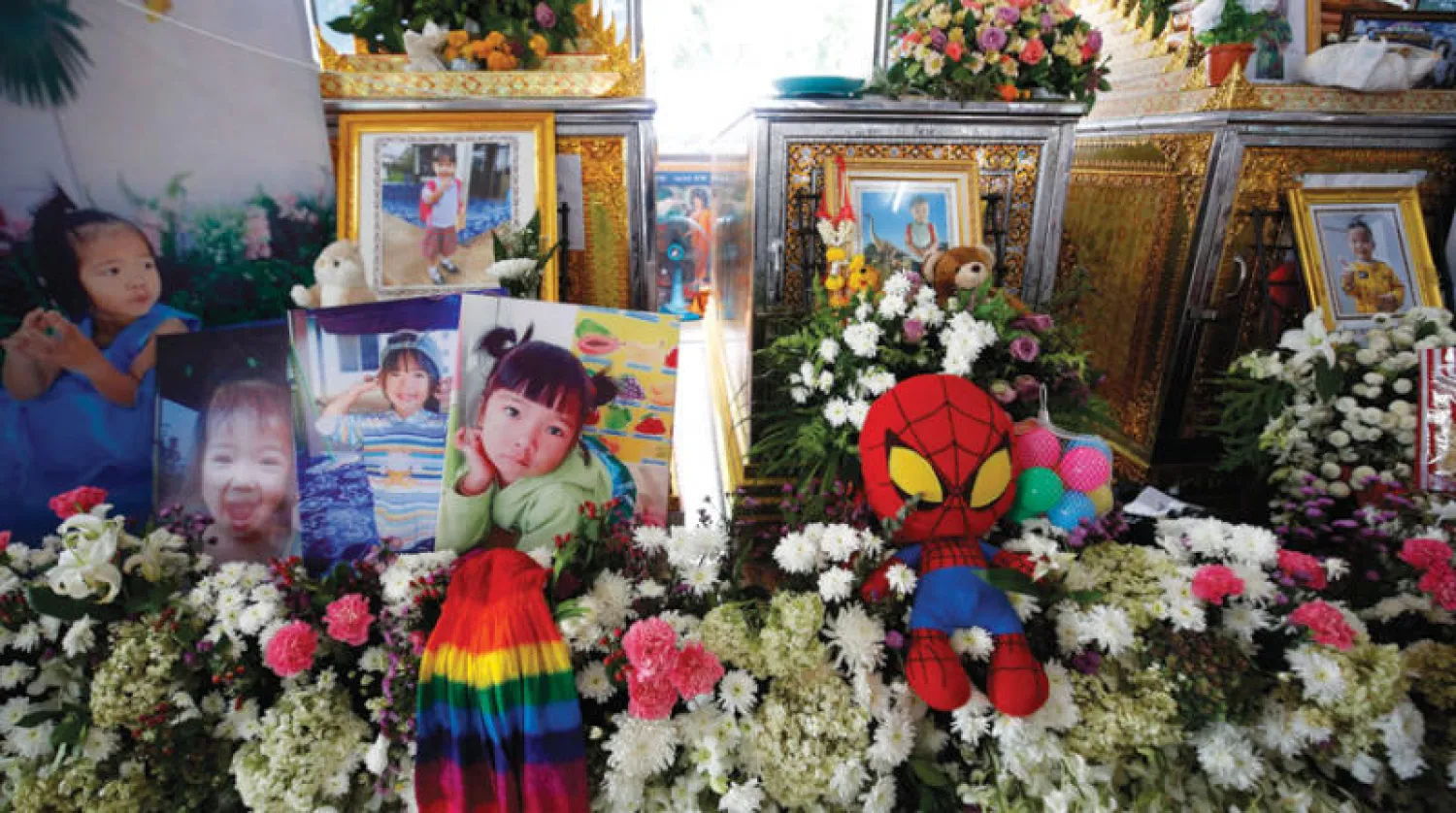 دمى وورود إلى جانب صور الأطفال الذين قضوا في الأسبوع الماضي أمام الحضانة التي شهدت الحادث (إ.ب.أ)