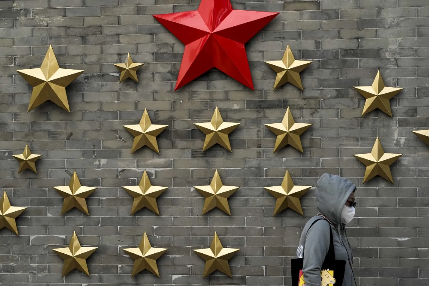 A woman wearing a face mask walks by communist symbol of a stars on display outside a restaurant in Beijing, Sunday, Oct. 9, 2022. (AP)