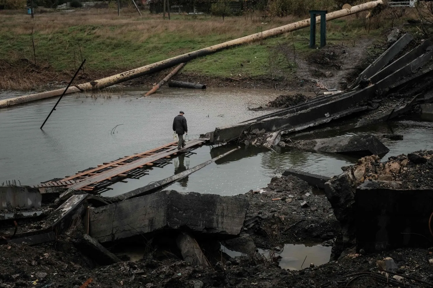 A man crosses the destroyed bridge with water bottles in the frontline town of Bakhmut in the Donetsk region on October 11, 2022, amid the Russian invasion of Ukraine. (AFP)