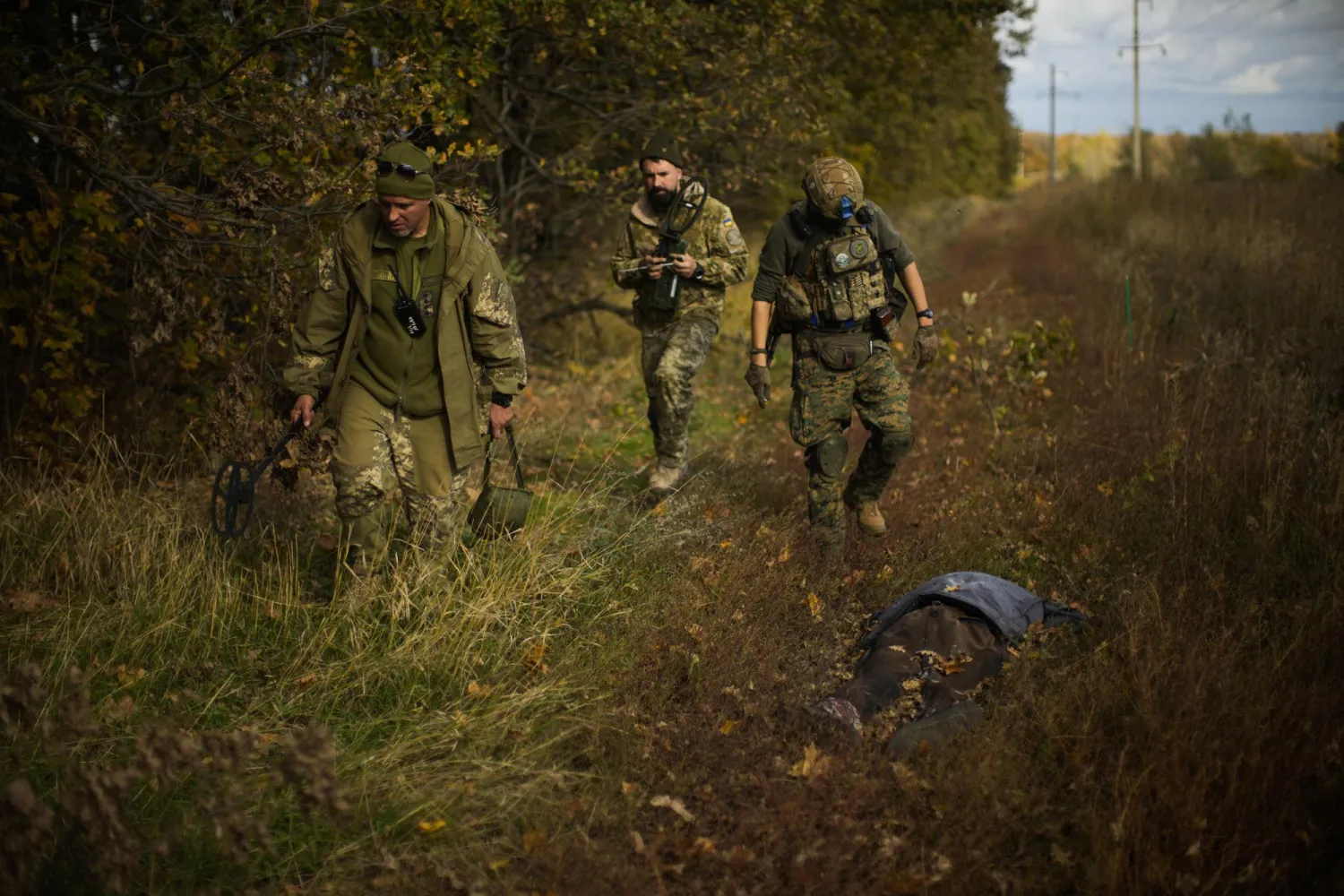 Ukrainian territorial defense deminers walk past a body of a local man who was killed after an explosion of a Russian mine near Grakove village, Ukraine, Thursday, Oct. 13, 2022. (AP Photo/Francisco Seco)
