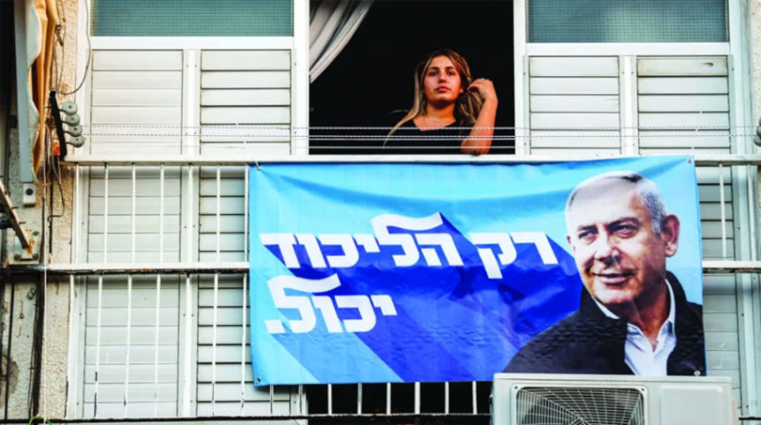 امرأة من الرملة تنظر من نافذة تعرض تحتها لافتة لحملة نتنياهو (رويترز)