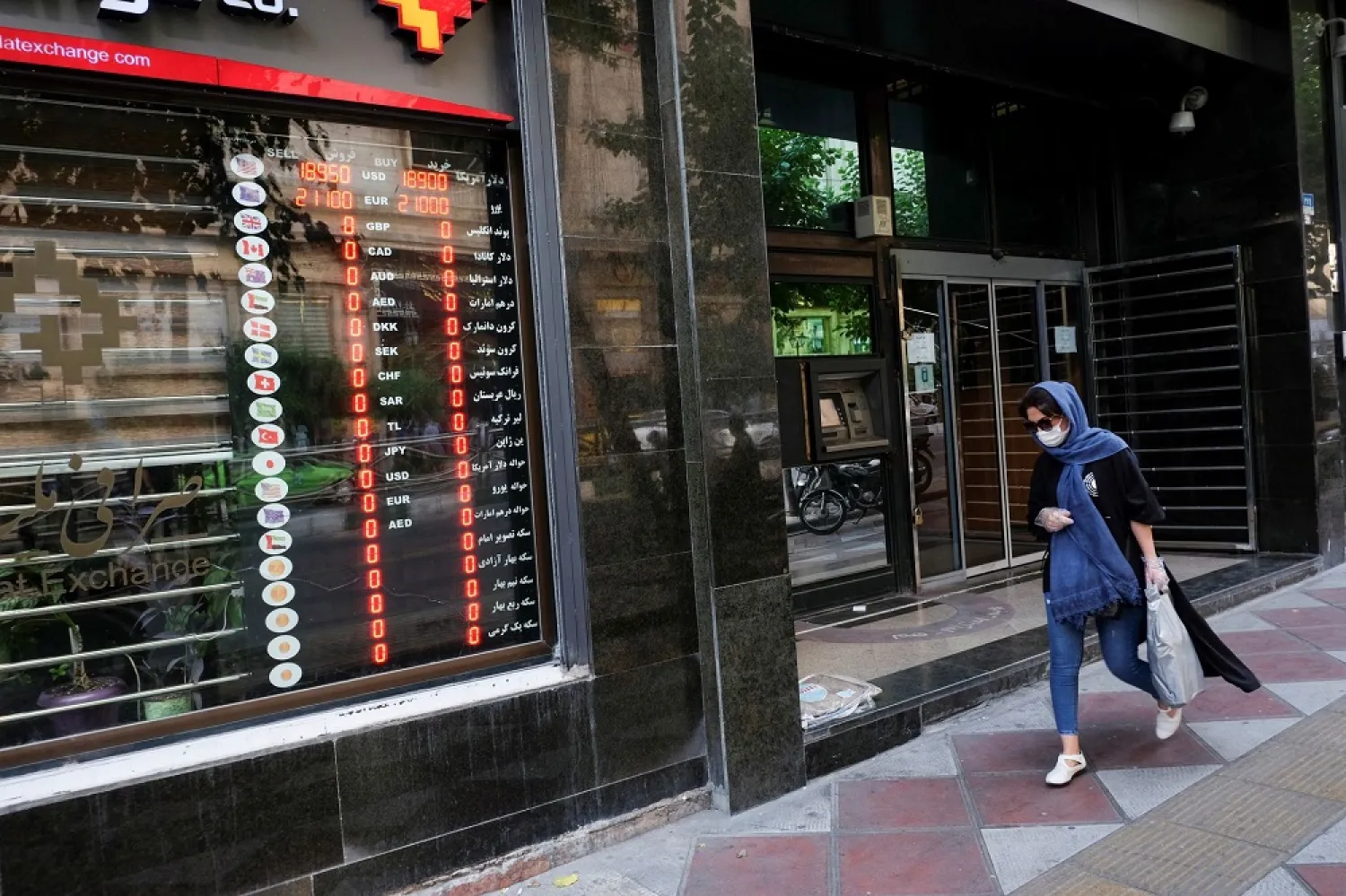 An Iranian woman wears a protective face mask as she walks next to an electronic currency board in Tehran, Iran July 2, 2020. Picture taken July 2, 2020. WANA (West Asia News Agency) via Reuters