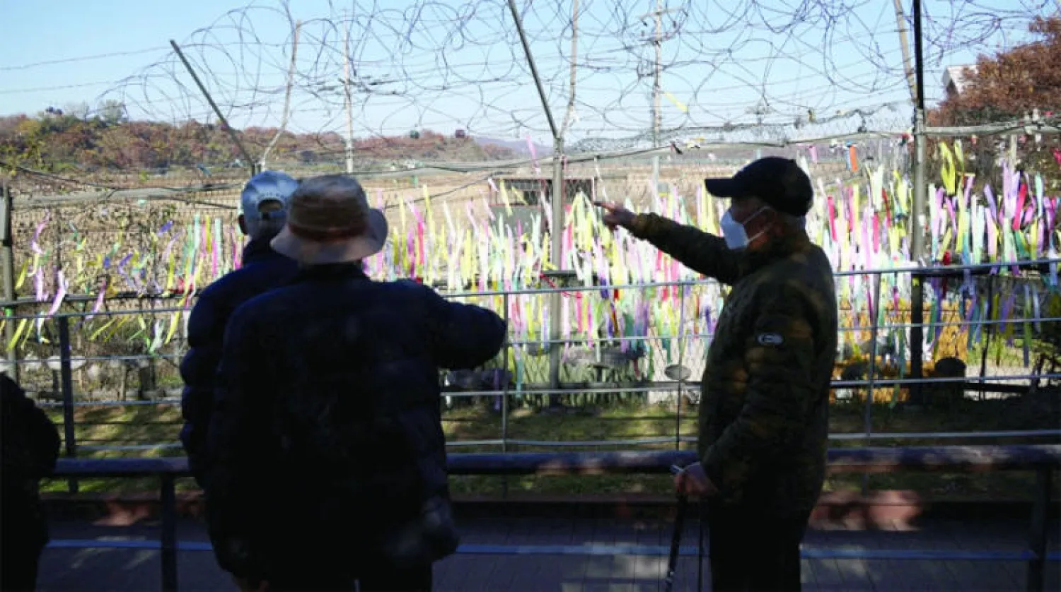 أشخاص يقفون عند السياج الحدودي في المنطقة المنزوعة السلاح بين الكوريتين الجمعة (رويترز)