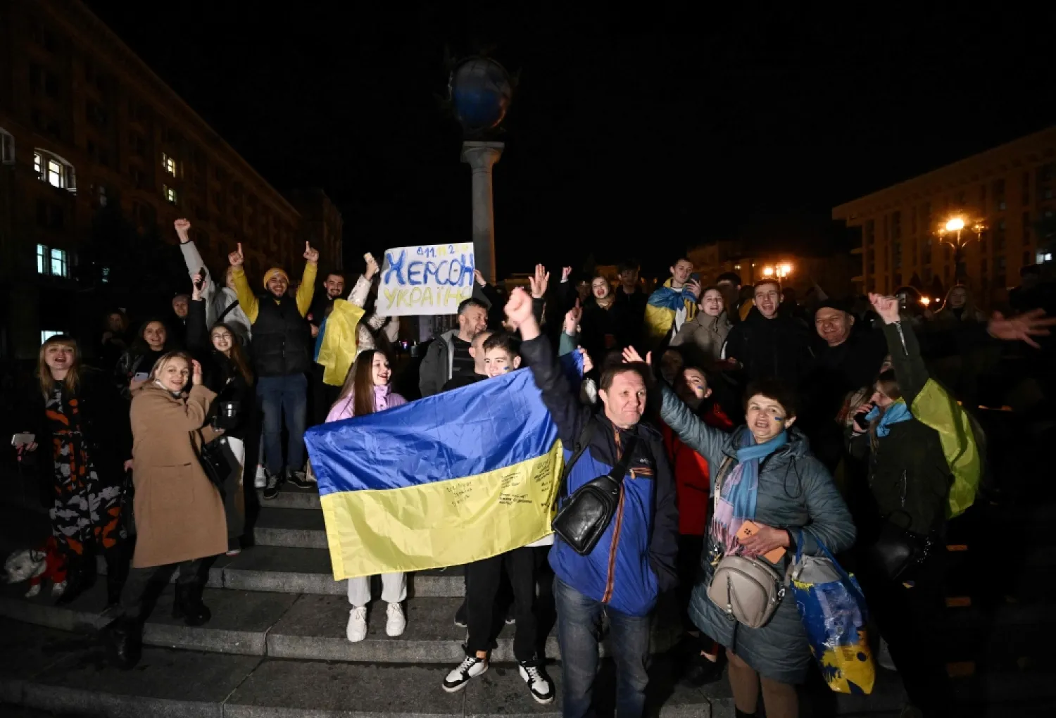 People hold a Ukrainian flag and a slogan which reads "11/11/2022 - Kherson - Ukraine" as they gather in Maidan Square to celebrate the liberation of Kherson, in Kyiv, on November 11, 2022. (AFP/Genya Savilov)

