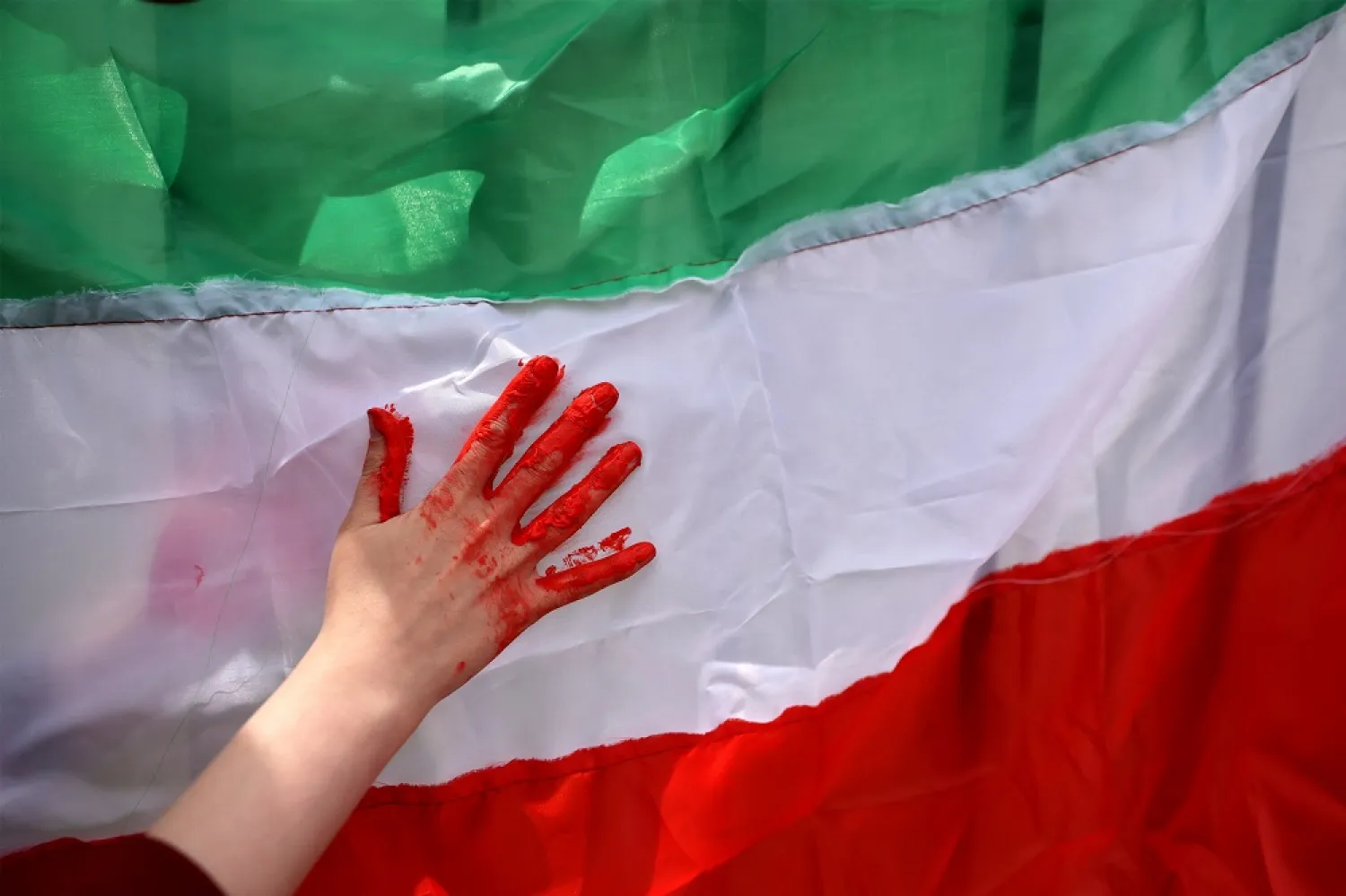 A  woman uses red paint on an Iranian flag as members of its community living in Chile protest outside the United Nations local headquarters in solidarity with Iranian people, in Santiago, Chile, November 11, 2022. (Reuters)
