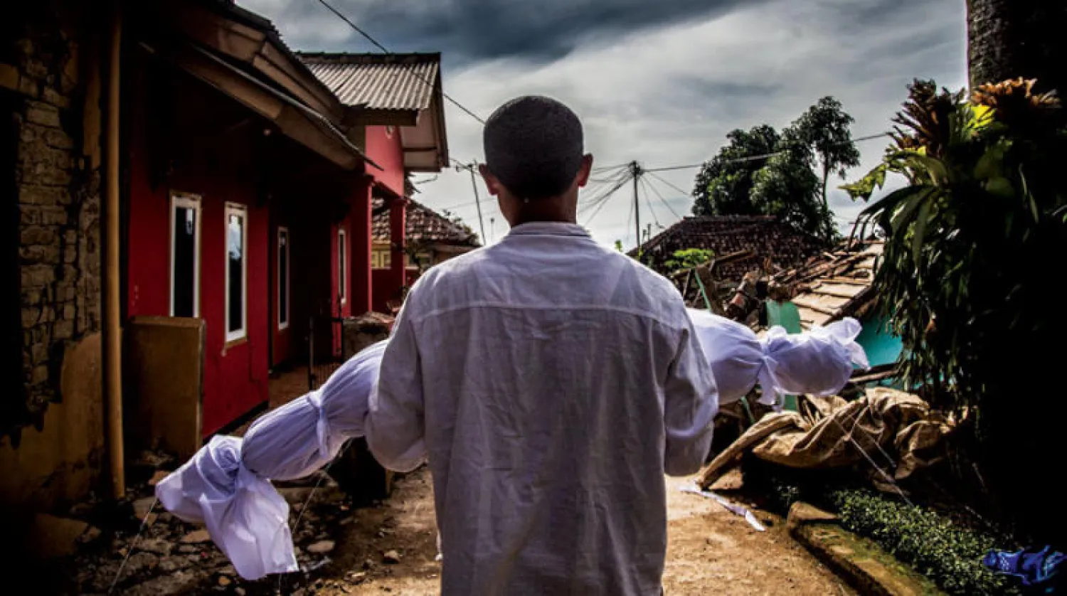 أب يحمل جثة ابنه ملفوفة في كفن أبيض وهو يسير في قريته التي ضربها الزلزال (أ.ف.ب)