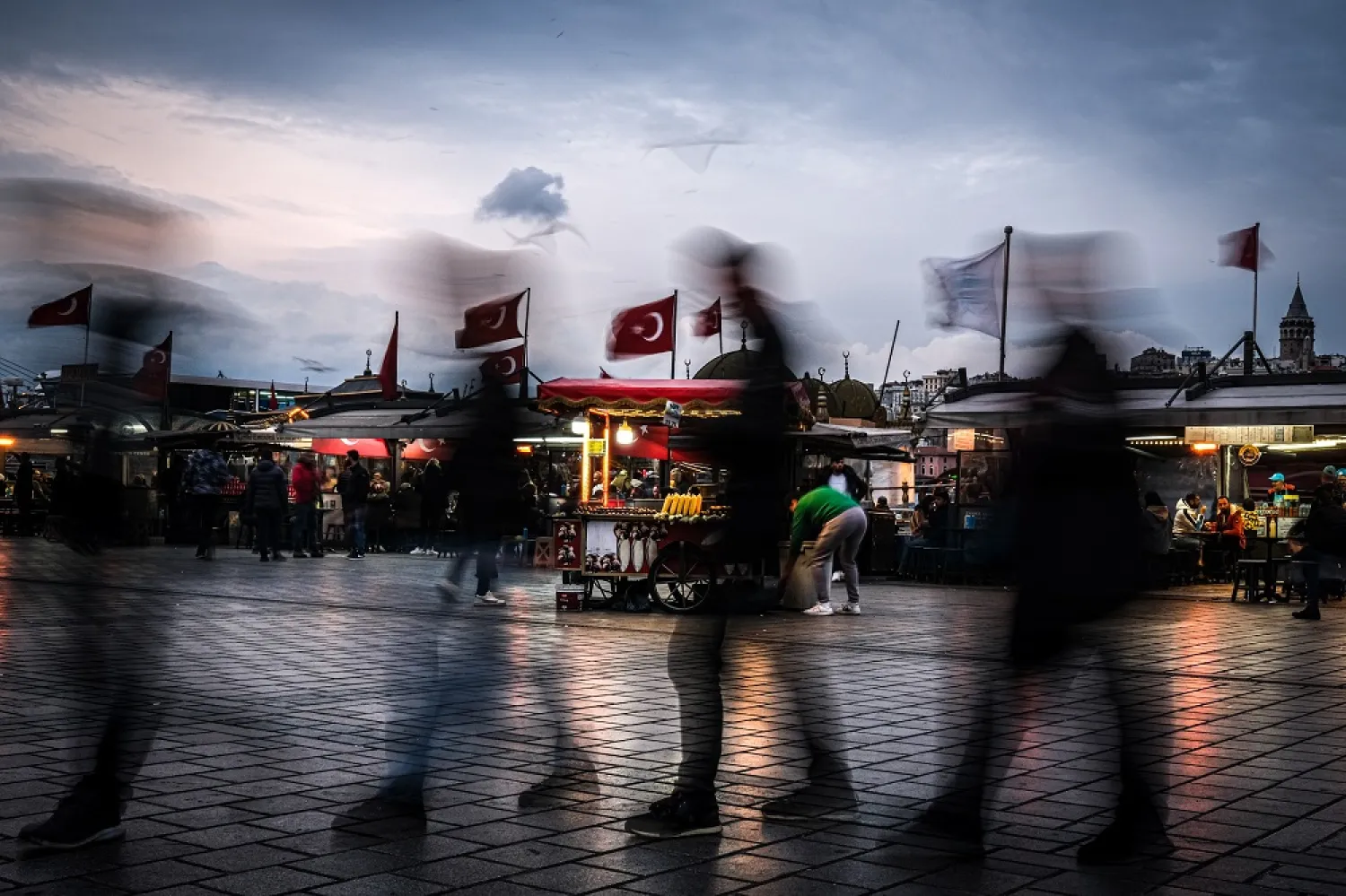 A slow shutter speed exposure of people walking in the famous touristy Eminonu Square with Galata tower (R) in the background during the sunset in Istanbul, Türkiye, 28 November 2022. (EPA)