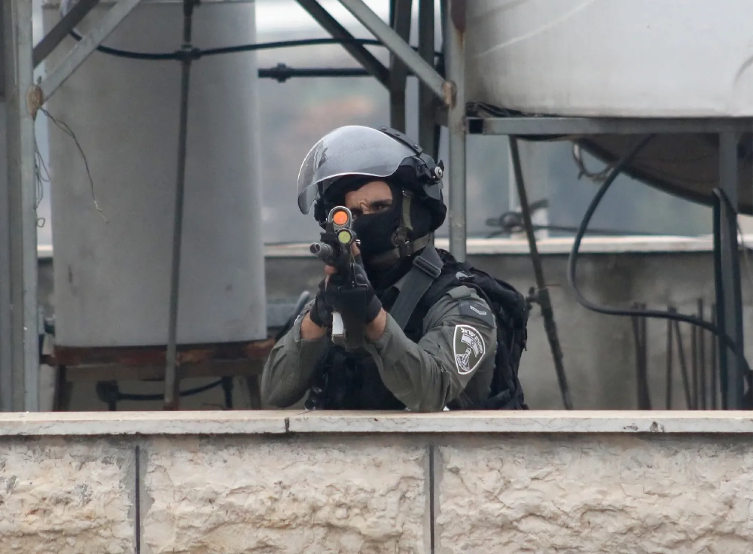 A member of Israeli security forces takes aim amid clashes with Palestinian protesters in the village of Beit Ummar, north of Hebron city in the occupied West Bank, on November 29, 2022, after the funeral of a Palestinian man who was killed earlier during clashes with Israeli forces. (AFP)