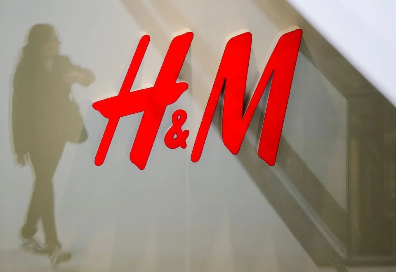 A woman is reflected next to the logo of the H&M fashion retailer in the newly opened Mall of Berlin shopping center in Berlin, Germany, in this September 25, 2014 file photo. REUTERS/Thomas Peter