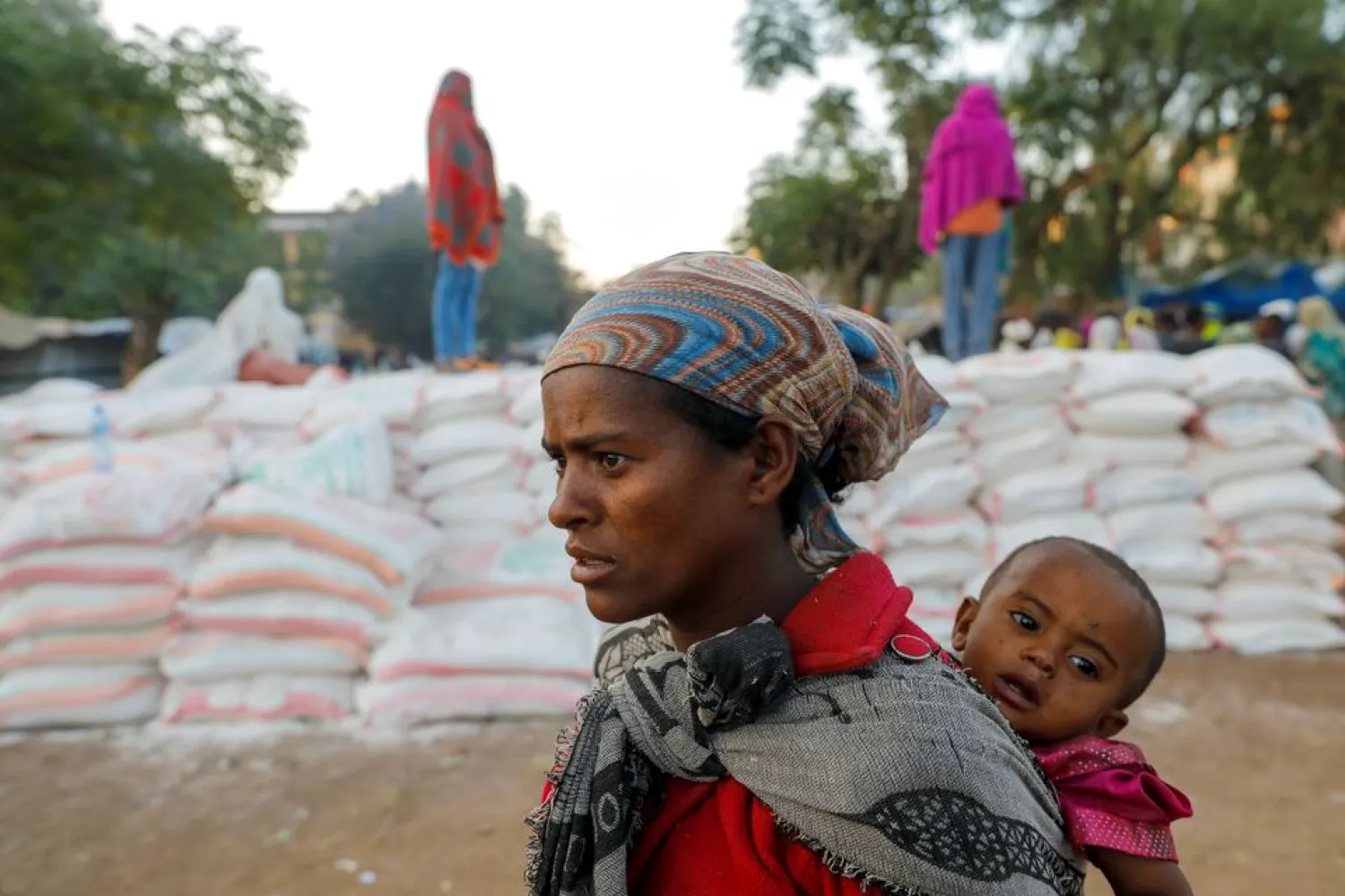 A woman carries an infant as she queues in line for food, at the Tsehaye primary school, which was turned into a temporary shelter for people displaced by conflict, in the town of Shire, Tigray region, Ethiopia, March 15, 2021. REUTERS/Baz Ratner/File Photo