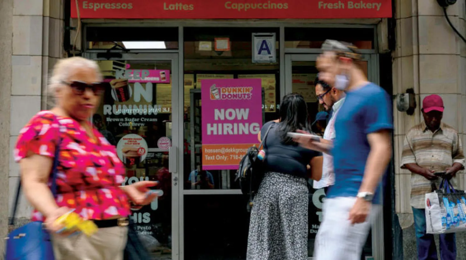 أميركيون يمرون بجانب محل في مدينة نيويورك الأميركية عليه لافتة تقول «لدينا وظائف الآن» (أ.ف.ب)