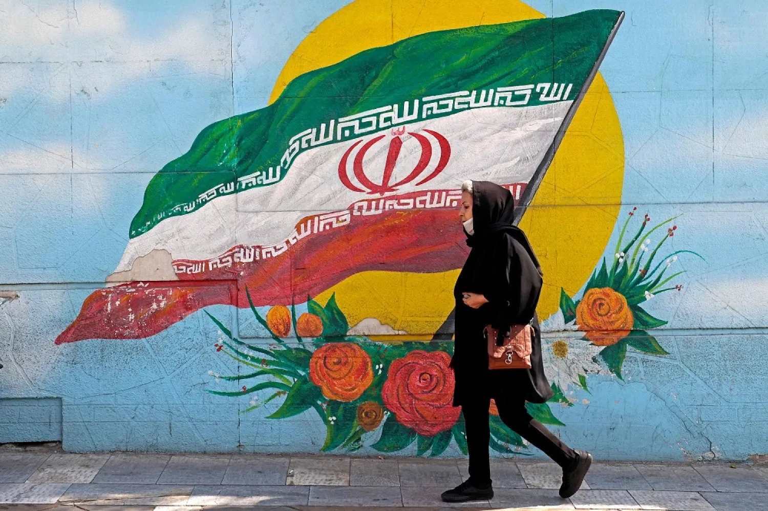 In this file photo taken on October 11, 2022, a woman walks past a mural in the Iranian capital Tehran. (AFP)