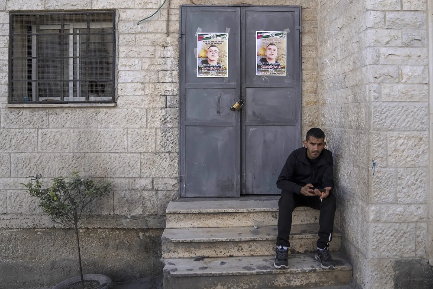 A Palestinian man sits in front of doors plastered with posters showing Ammar Adili, 22, who was shot and killed by an Israeli border police officer on Friday, in his home village of Osreen, south of the West Bank city of Nablus, Saturday, Dec. 3, 2022. (AP)