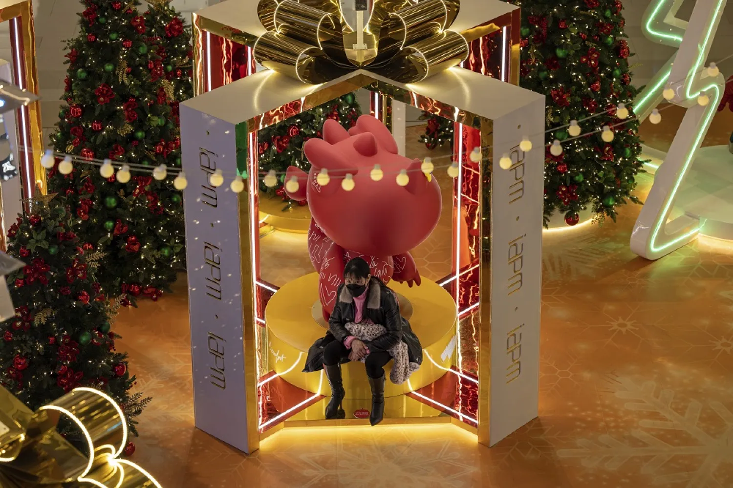 A woman wearing a mask rest near Christmas decorations at a mall in Shanghai on Friday, Dec. 16, 2022. (AP)