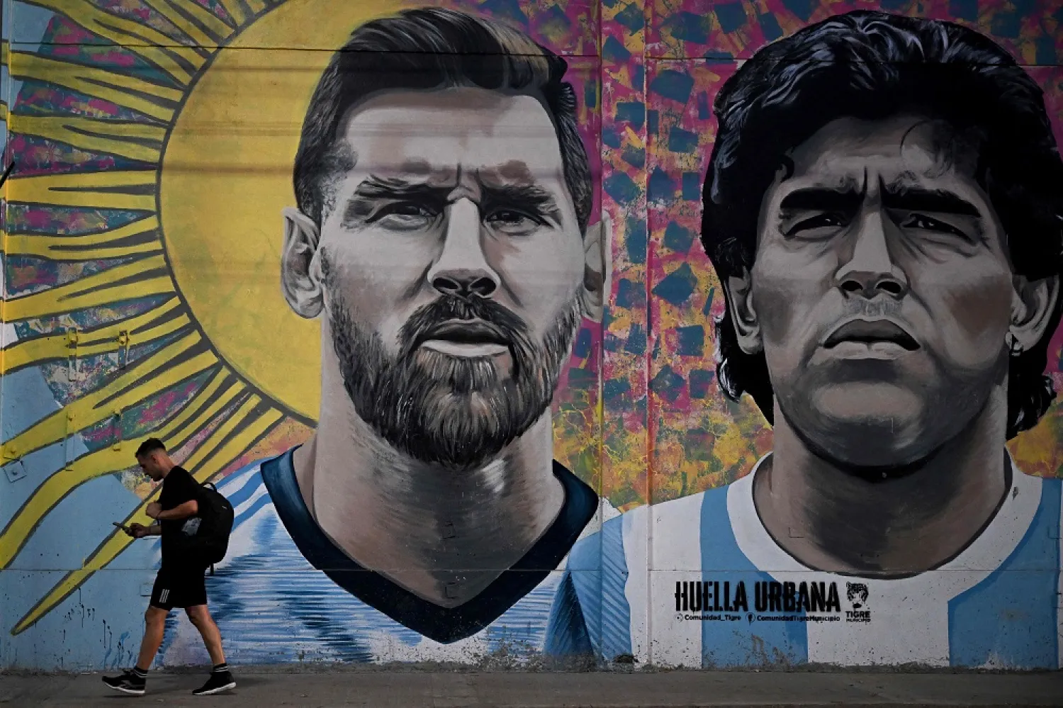 A man passes by a mural depicting Argentine football stars Lionel Messi (L) and late Diego Maradona (R) in the eve of Qatar 2022 World Cup final football match between Argentina and France in Buenos Aires, on December 16, 2022. (AFP)
