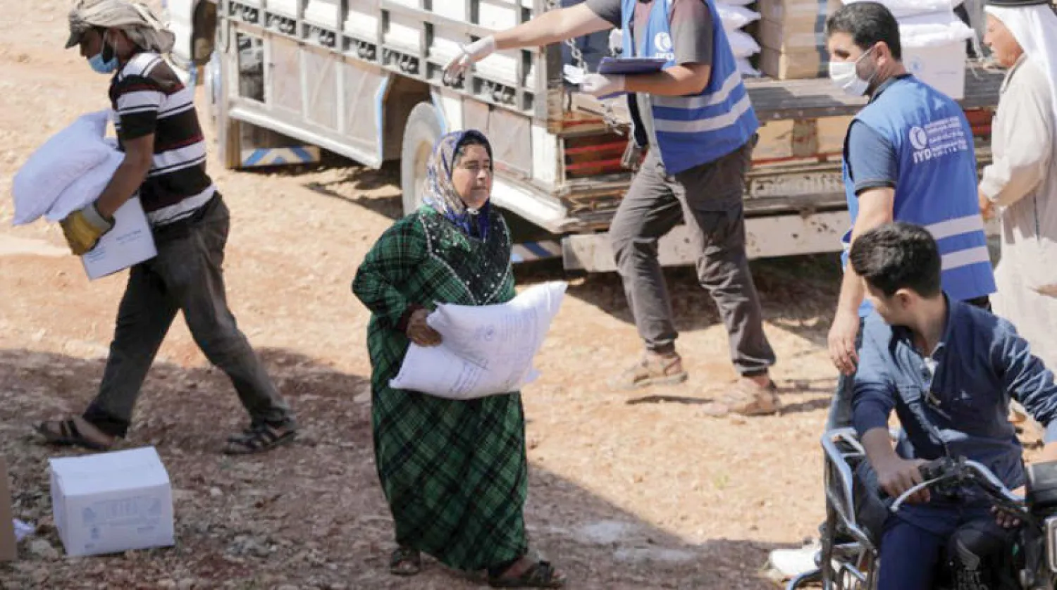 نازحة سورية في مدينة إدلب تحمل حقيبة مساعدات إنسانية يونيو 2021 (رويترز)