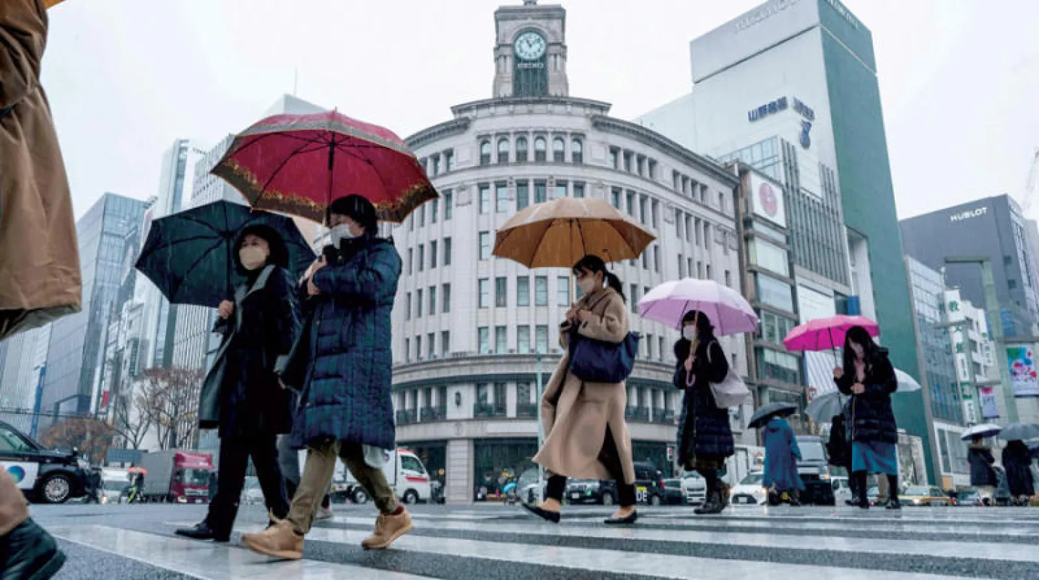 مشاة يعبرون شارعاً وسط الأمطار في العاصمة اليابانية طوكيو (أ.ف.ب)