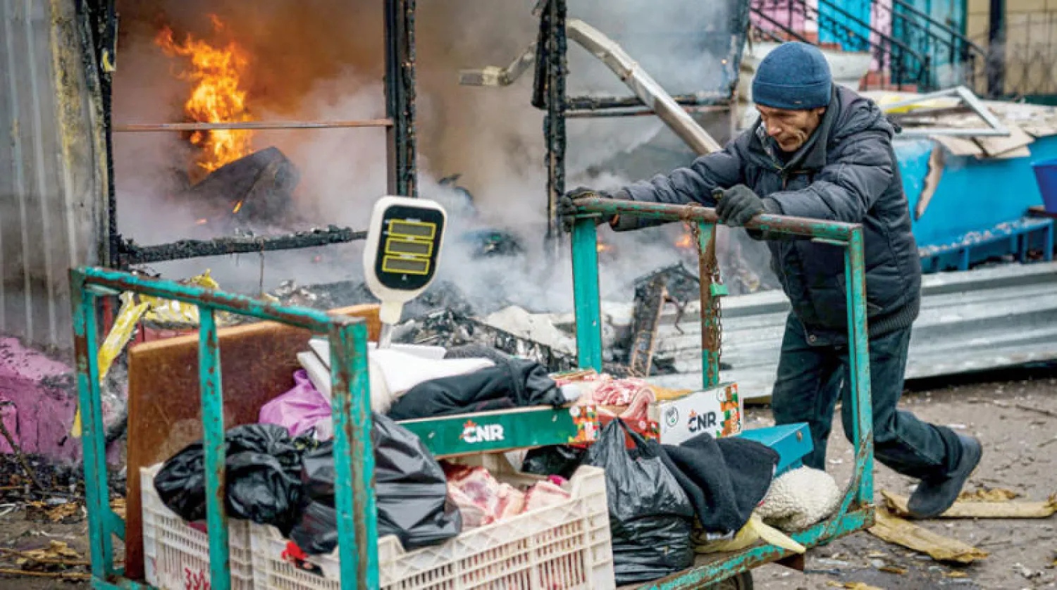 أوكراني يدفع بعربته قرب متجر احترق جراء القصف في خيرسون (أ.ف.ب)