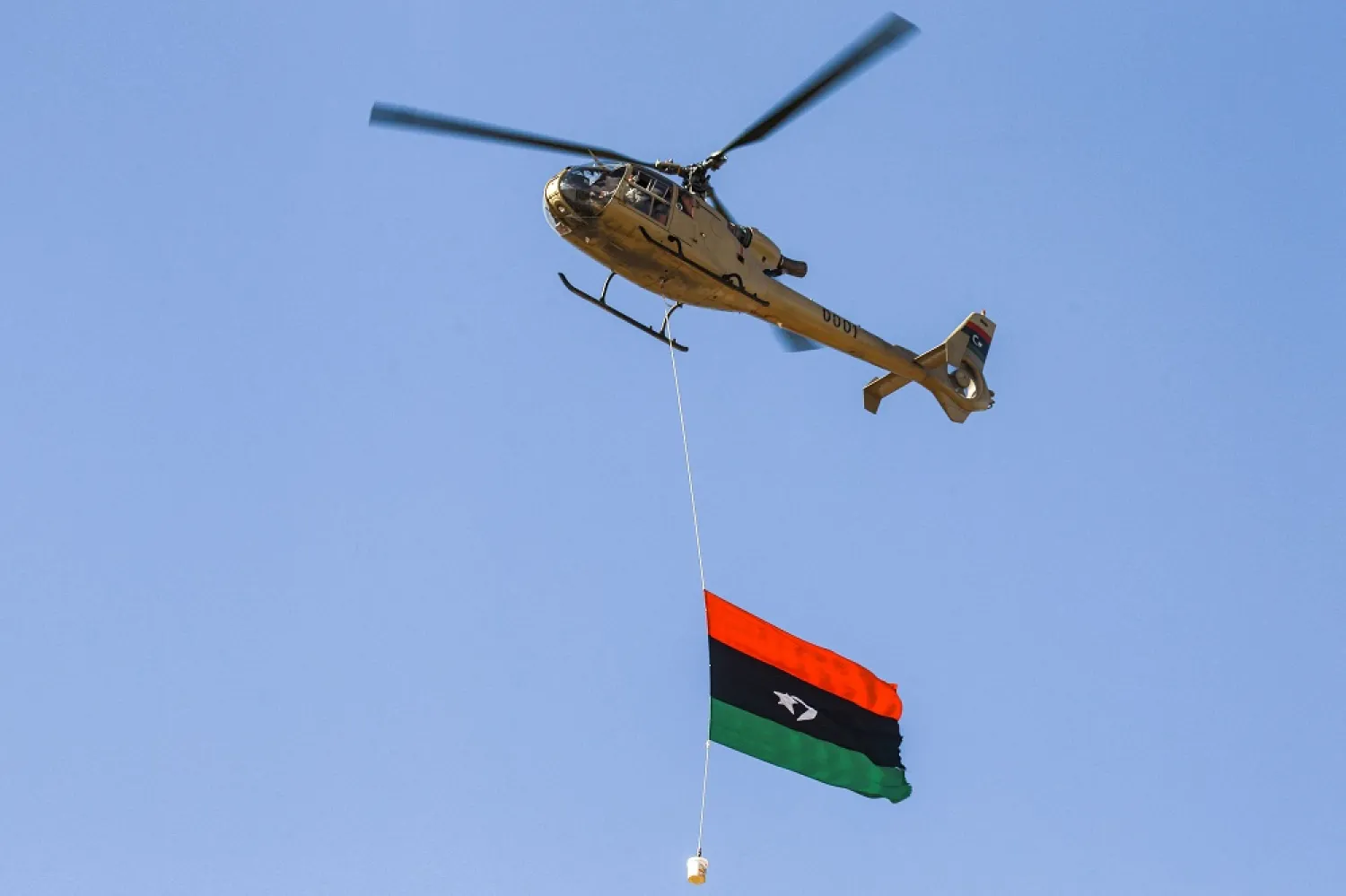A military helicopter flies with a Libyan national flag hanging underneath at a rally marking the 71st anniversary of the country's independence from Italy in the eastern city of Benghazi on December 24, 2022. (AFP)