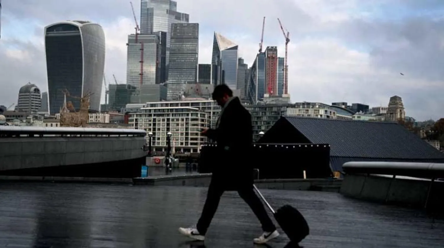 أحد المشاة يسير إلى جوار نهر التيمس مقابل الحي المالي في العاصمة البريطانية لندن (إ.ب.أ)
