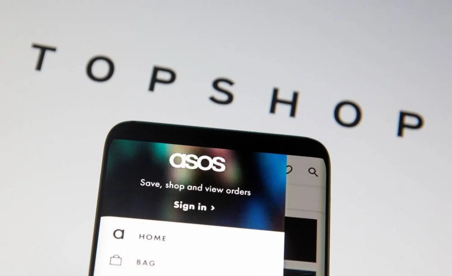 The ASOS logo is seen in a smartphone in front of a displayed TopShop logo in this illustration taken January 25, 2021. (Reuters)