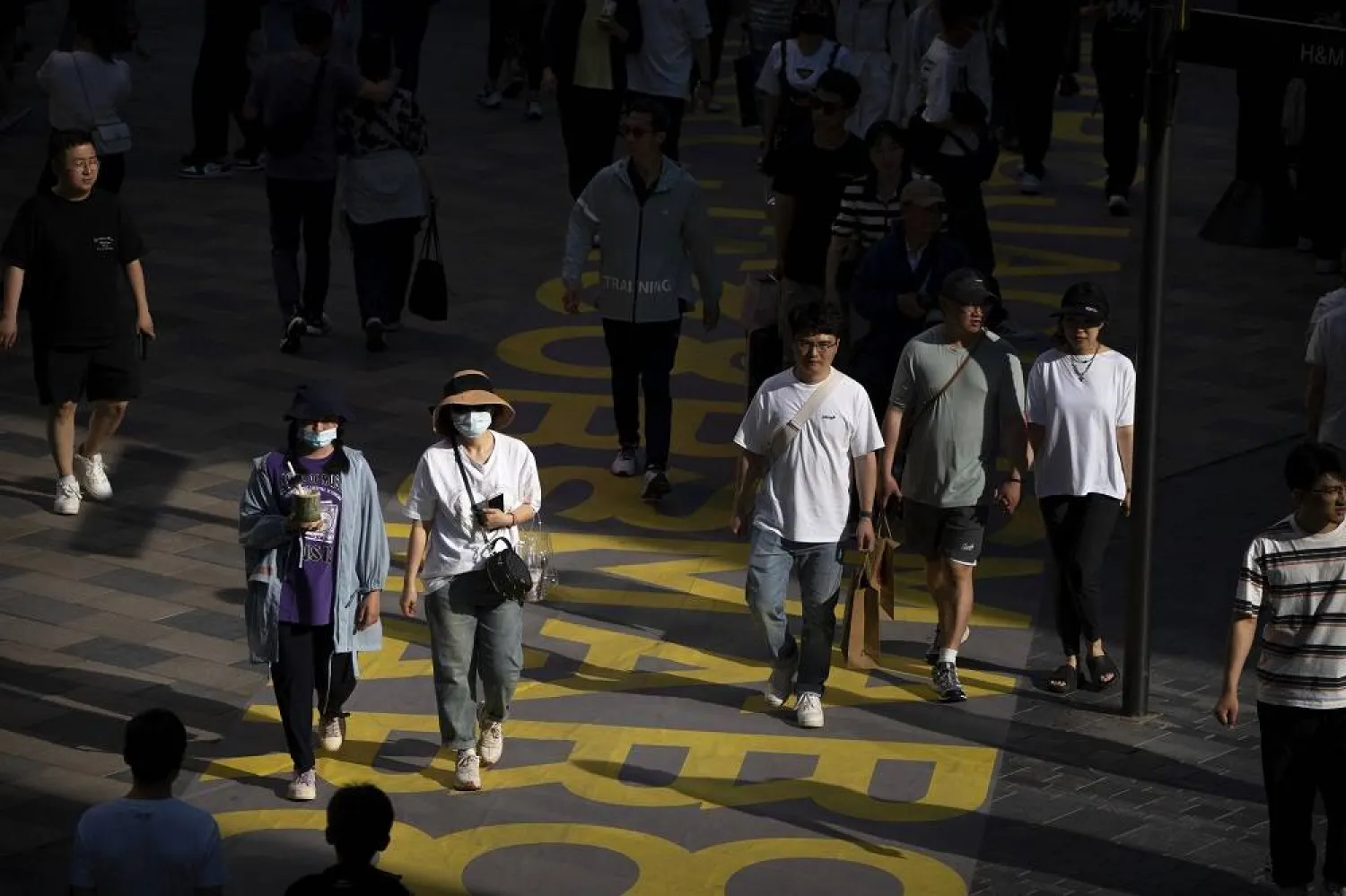 People wearing face masks walk at an outdoor shopping center in Beijing, Saturday, May 13, 2023. (AP)