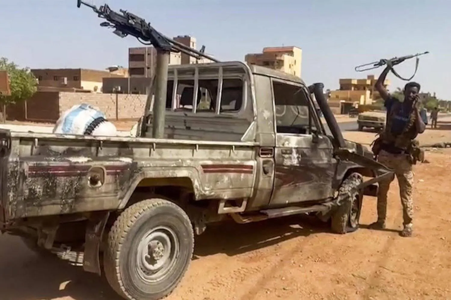 مقاتل يلوِّح ببندقية وهو يقف بجانب مركبة معطوبة في حي النيل بالخرطوم الكبرى (أ.ف.ب)
