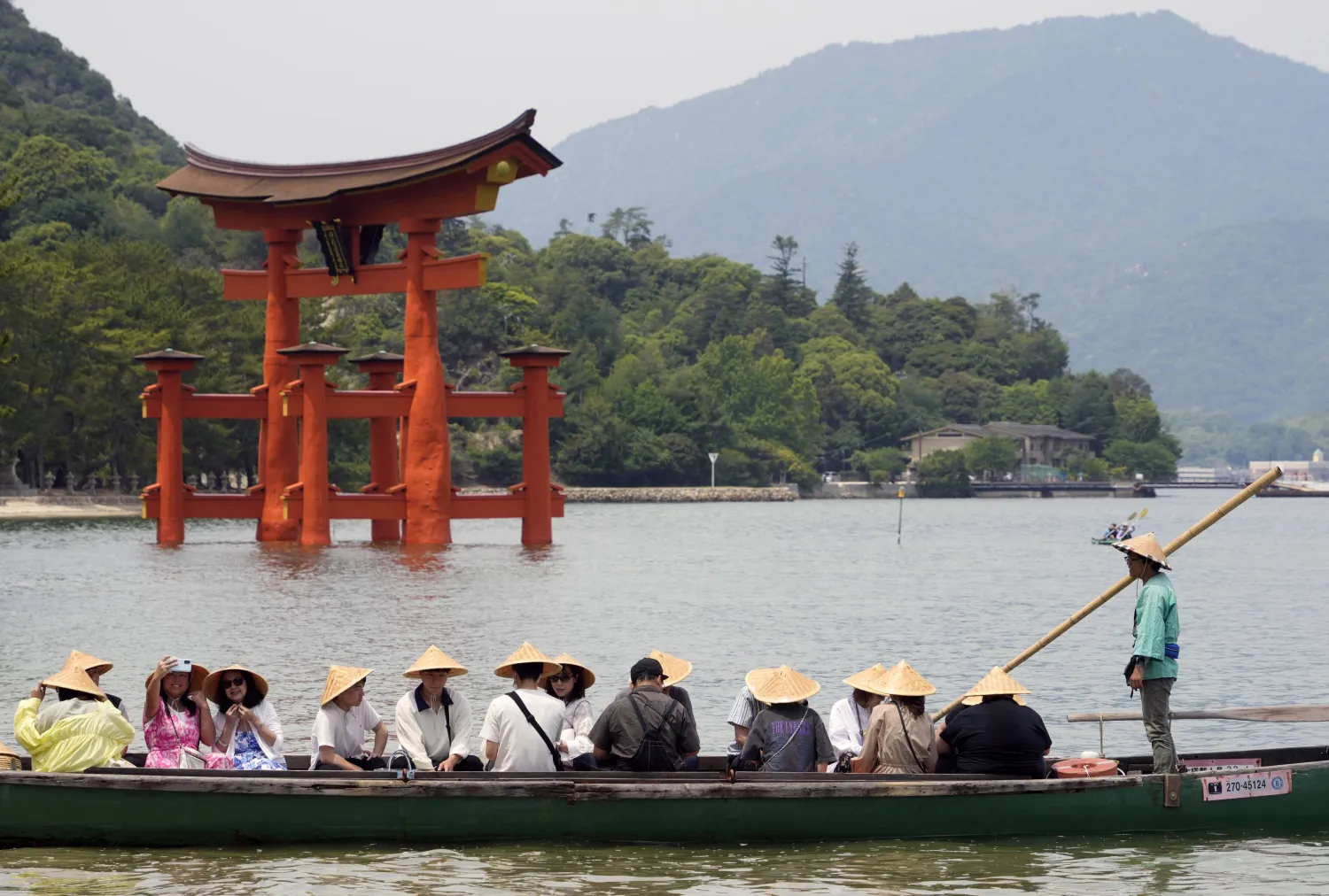 سائحون على مركب خشبي تقليدي يشاهدون نصب ايتسوكوشيما التذكاري على ساحل مدينة هيروشيما اليابانية (إ.ب.أ)