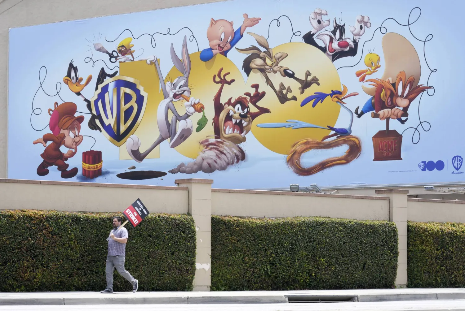 A picketer walks underneath a billboard highlighting Warner Bros. animated characters during a Writers Guild rally, Monday, May 22, 2023, outside Warner Bros. Studios in Burbank, Calif. (AP Photo/Chris Pizzello)