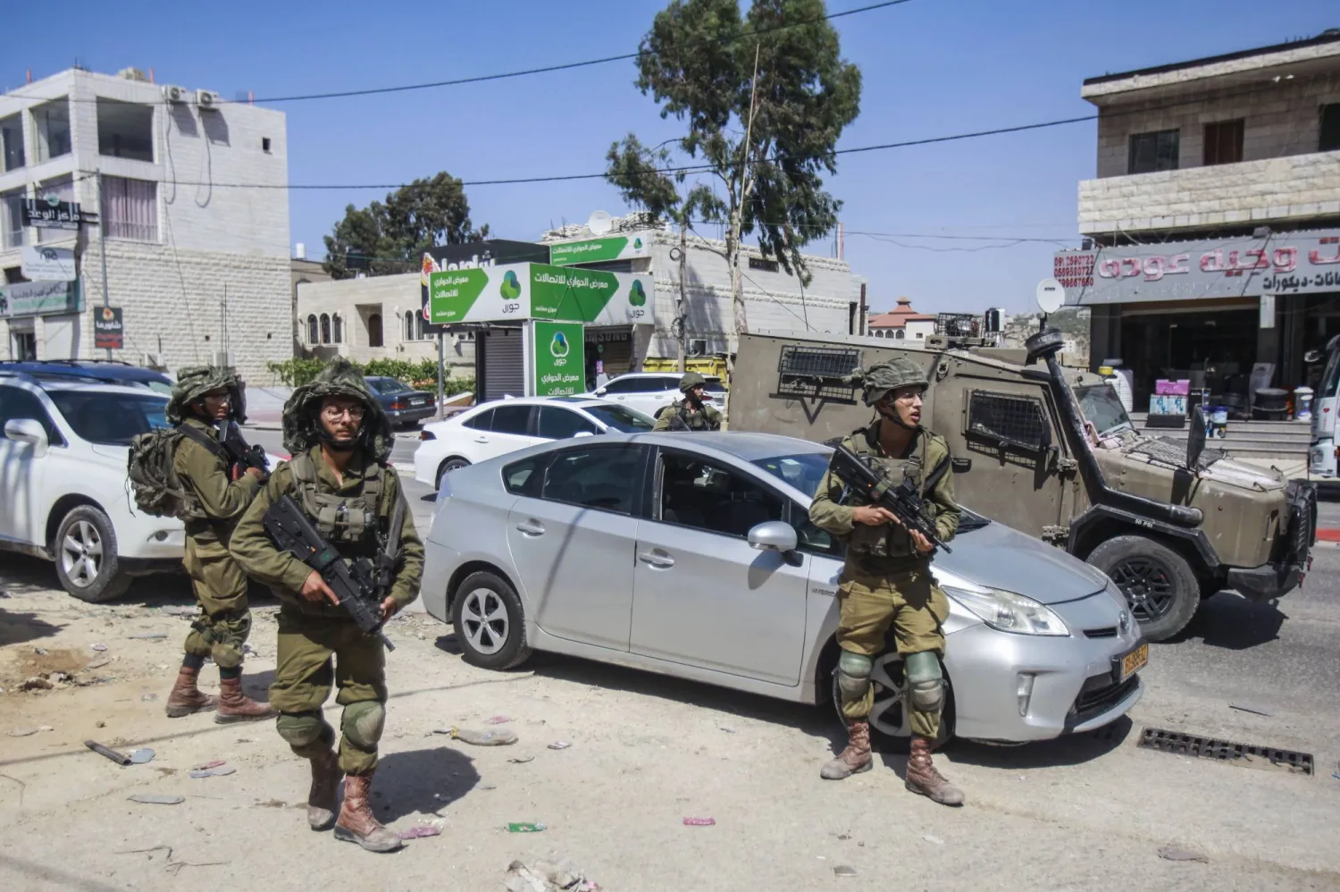 جنود إسرائيليون يحرسون أمس الثلاثاء سيارة لأحد المستوطنين رُشقت بالحجارة في بلدة حوارة جنوب نابلس بالضفة الغربية (د.ب.أ)