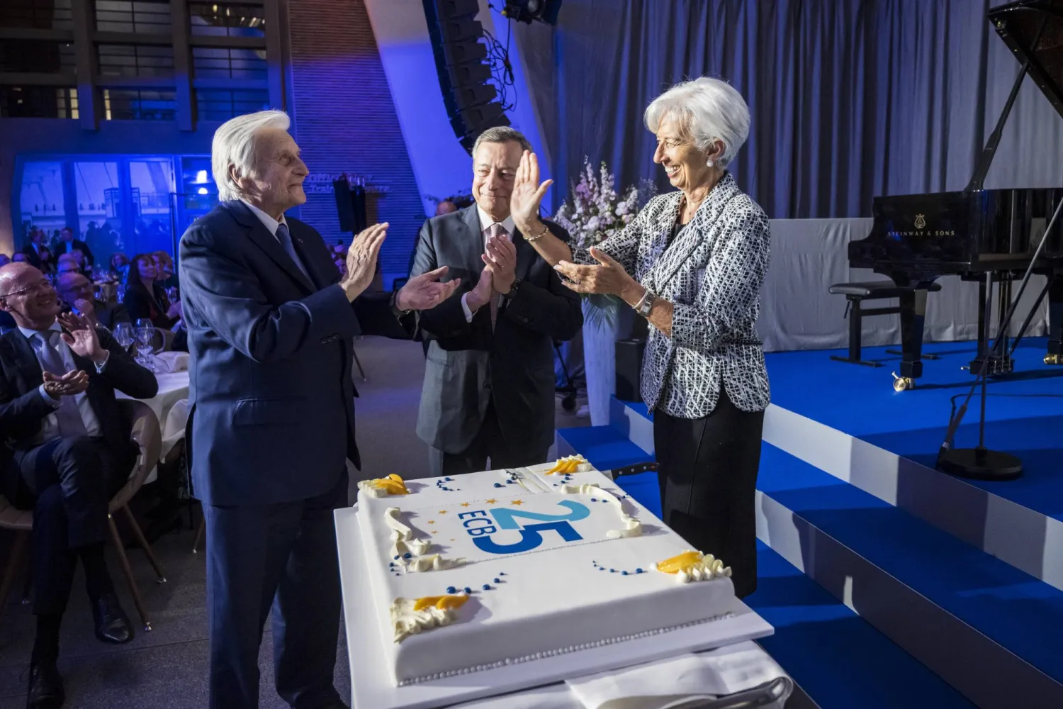 رئيسة البنك المركزي الأوروبي كريستين لاغارد ترحب بالرؤساء السابقين جان كلود تريشيه (يسار) وماريو دراغي (وسط) أمام كعكة الاحتفال باليوبيل الفضي للبنك في مدينة فرانكفورت (إ.ب.أ)