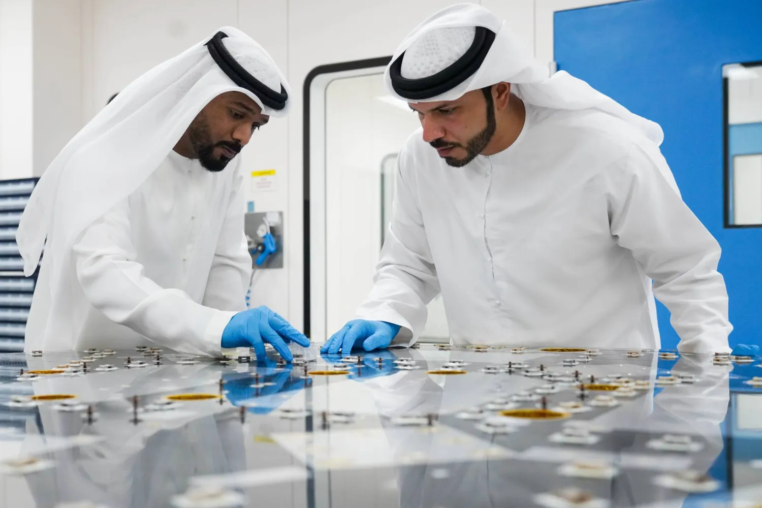 موظفان في شركة ستراتا للتصنيع يفحصان أحد مكونات الأقمار الاصطناعية المصنعة محليًا (وام)