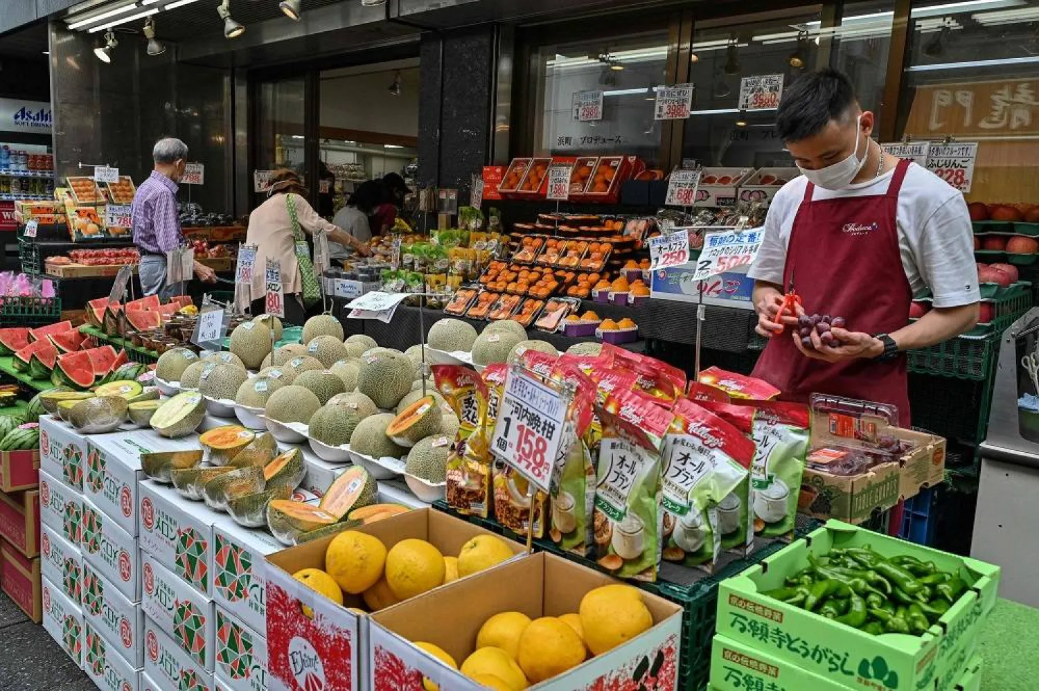 An employee (R) cuts fruit as shoppers visit a market in Tokyo on June 6, 2023. (AFP) 