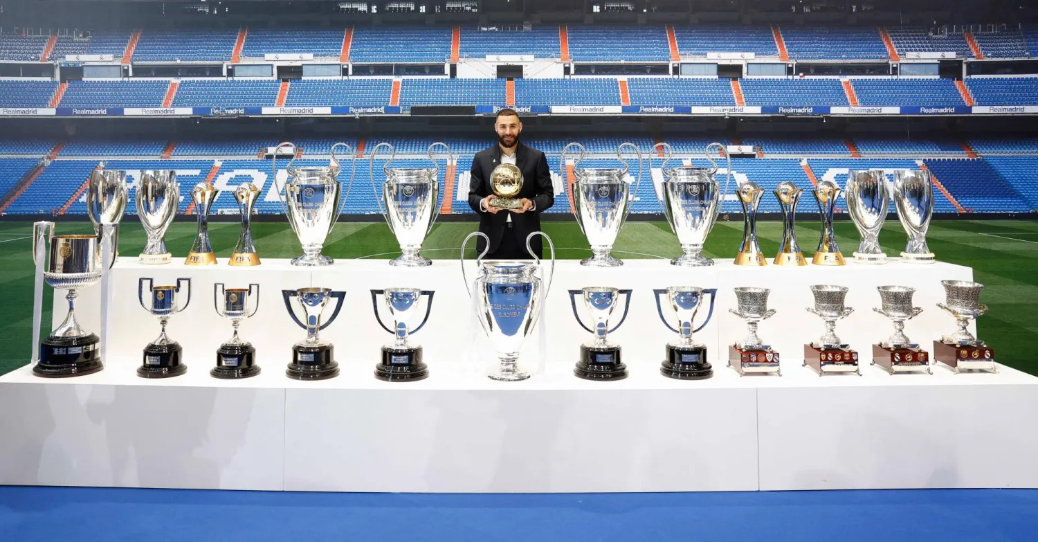 بنزيمة في وداعه ريال مدريد مع الكؤوس والجوائز التي حصدها مع النادي الإسباني (أ.ف.ب)