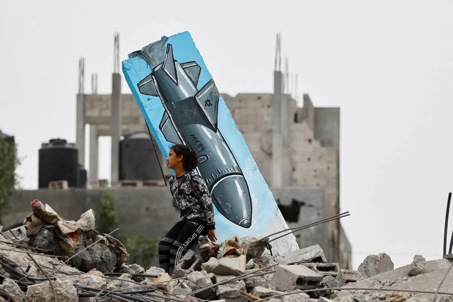 A Palestinian girl sits on the remains of a destroyed house, next to a graffiti of a missile drawn by Hussein Abu Sadeq, on houses destroyed by Israel in recent Israeli-Gaza fighting, in Deir Al-Balah, central Gaza Strip June 8, 2023. (Reuters)