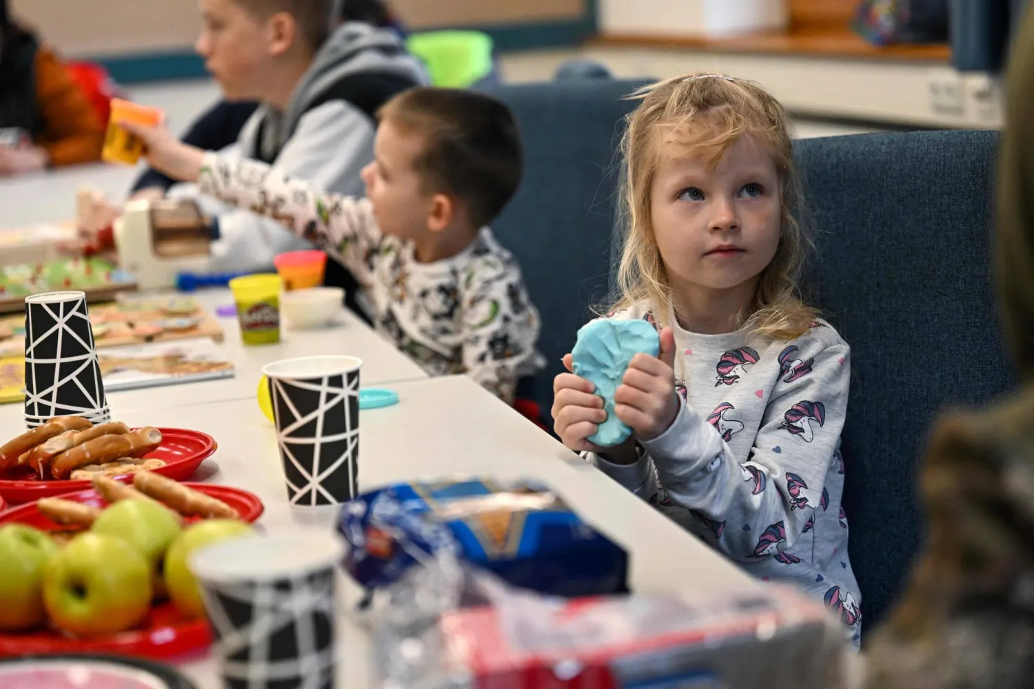 طفلة أوكرانية تستمع مع والديها إلى محاضرة تلقيها اللاجئة الأوكرانية في المجر أولينا أندريتشوك حول برنامج علاجي لمساعدة الصغار ذوي الإعاقة القادمين من أوكرانيا (أ.ف.ب)