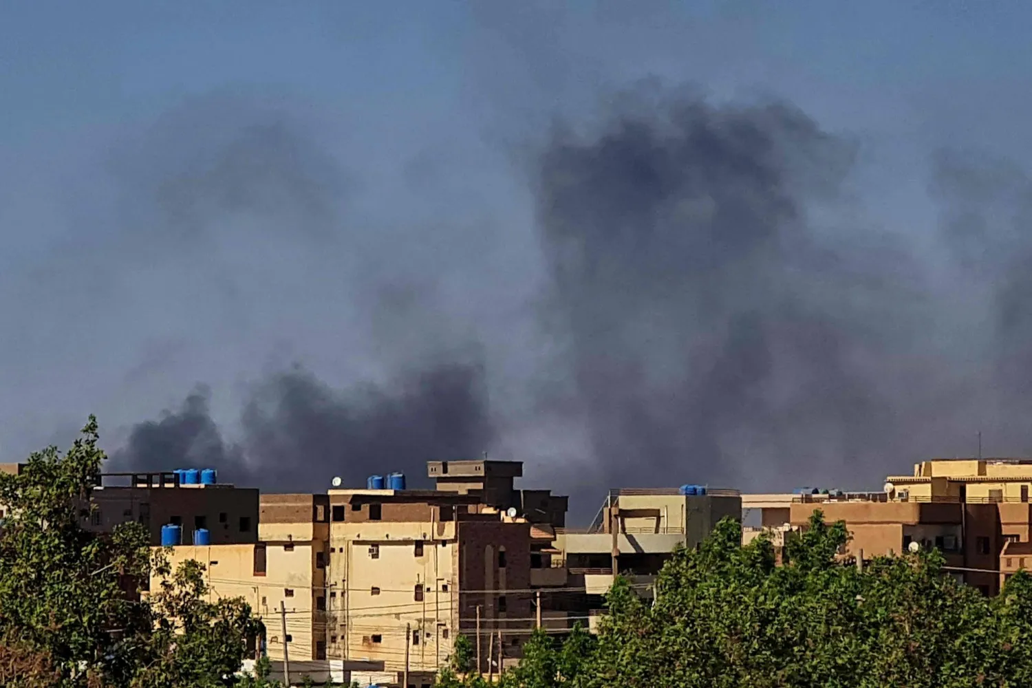 الدخان يتصاعد خلف المباني وسط استمرار القتال في السودان (أ.ف.ب)