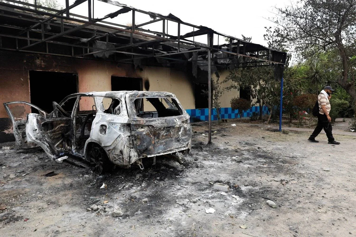 رجل يمر أمام مركز شرطة متضرر أضرمت فيه النيران خلال اشتباكات بين الشرطة وأنصار رئيس الوزراء الباكستاني السابق عمران خان في إسلام آباد (رويترز)