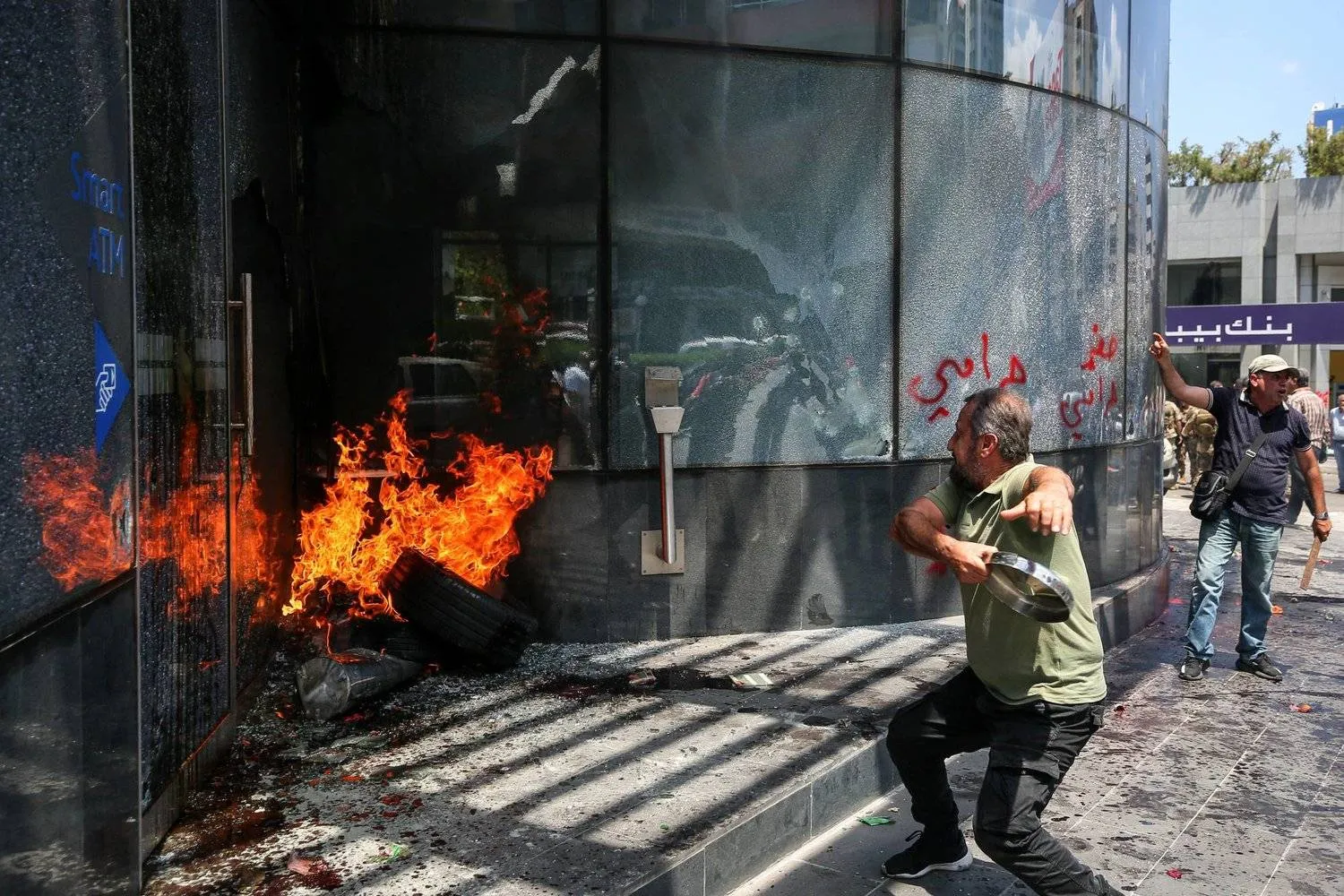 15 June 2023, Lebanon, Beirut: A Lebanese depositor hurls a metal piece at a local bank's facade in the Sin el-Fil suburb east of Beirut. Dozens of Lebanese protesters on Thursday attacked major banks in the nation's capital amid anger over a deepening economic crisis. Photo: Marwan Naamani/dpa