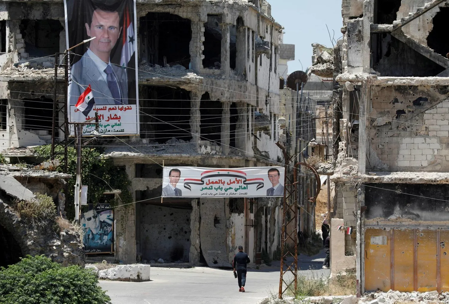 Suriye'nin Humus şehrinde savaştan zarar gören binaların önünde yürüyen bir kişi (Reuters-Arşiv)