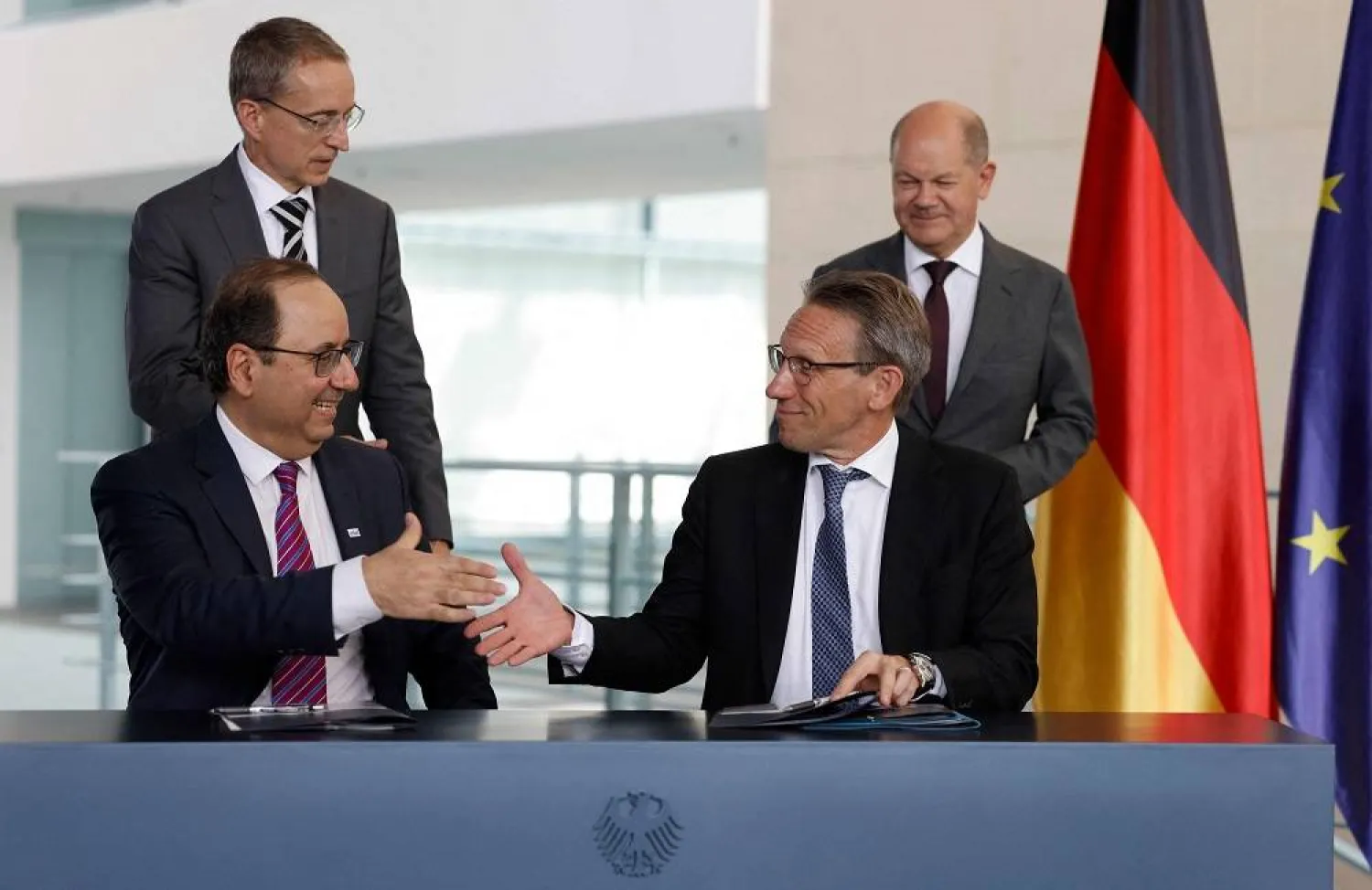 Pat Gelsinger (background L), CEO of US multinational corporation and technology company Intel, and German Chancellor Olaf Scholz (background R) look on as State Secretary at the Chancellery Joerg Kukies (foreground R) and Intel Executive Vice President Keyvan Esfarjani (foreground L) shake hands after they signed an agreement between the German government and Intel on June 19, 2023 at the Chancellery in Berlin. (AFP) 