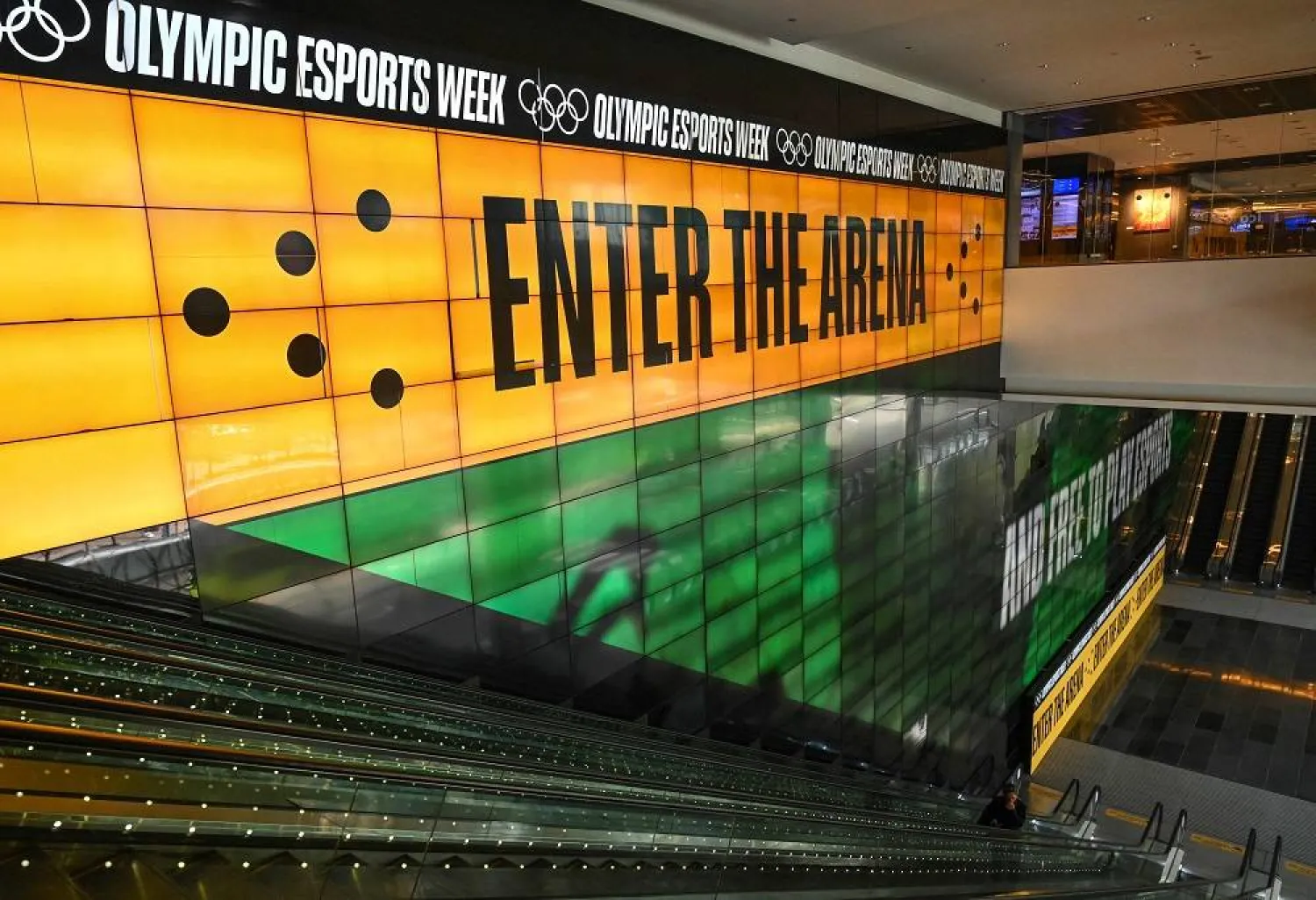 This photo taken on June 19, 2023 shows people standing in front of a digital screen displaying a banner for the Olympic Esports week at Suntec City convention and exhibition hall in Singapore. (AFP) 