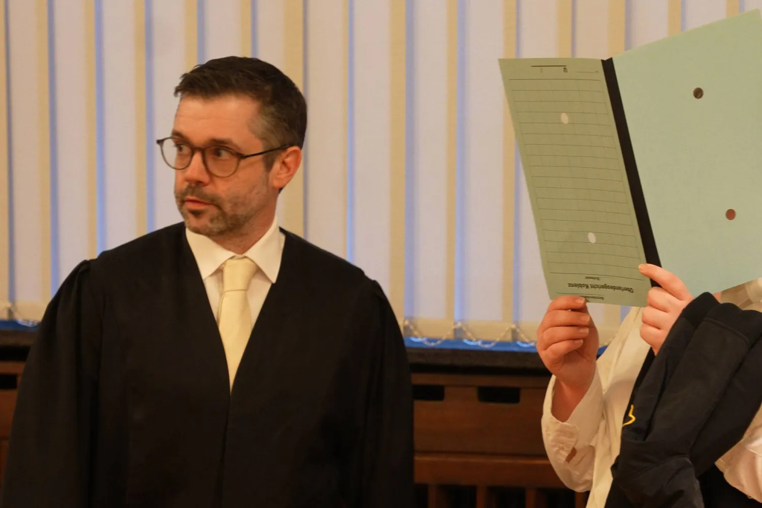 المتهمة تخفي وجهها بملف في محكمة كوبلنتس، وإلى جانبها أحد محاميها (د.ب.أ)