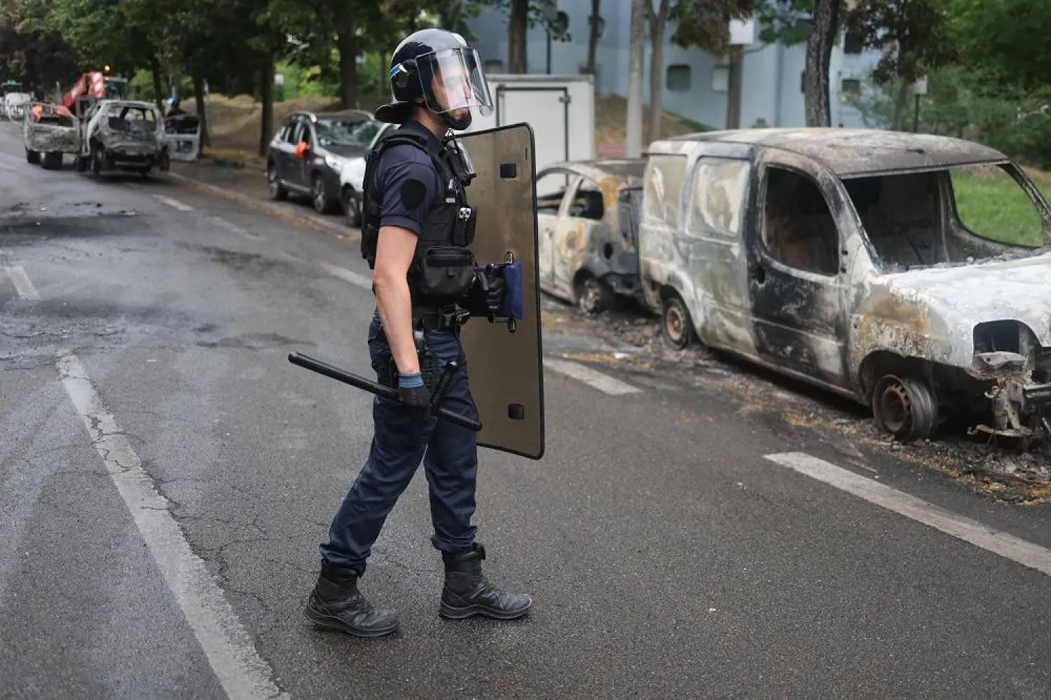 A French police officer in riot gear looks on next to burnt cars at the Pablo Picasso neighborhood in Nanterre on July 1, 2023, after a fourth consecutive night of rioting in France over the killing of a teenager by police. (AFP)