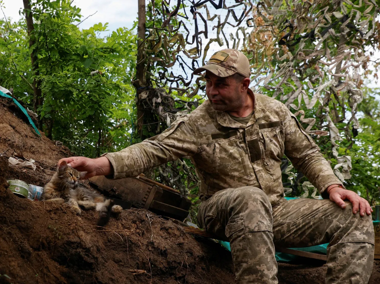 جندي أوكراني يداعب قطة في قرية نوفودارفيكا التي استعادت أوكرانيا السيطرة عليها مؤخراً (رويترز)