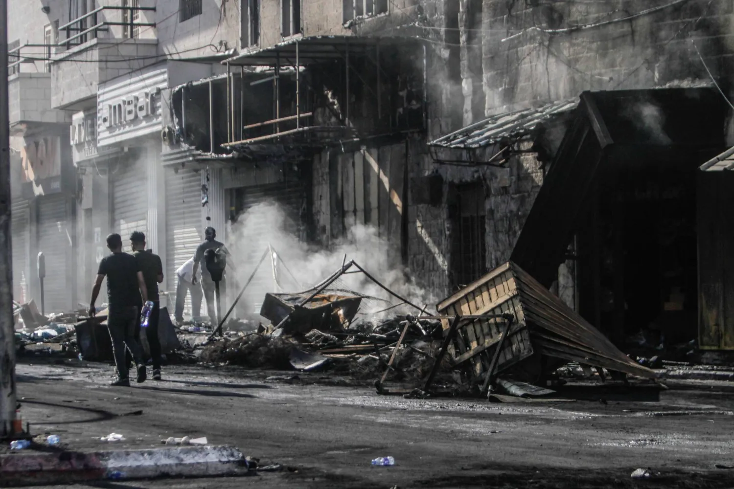 فلسطينيون يتفقدون محال تجارية وسط جنين أحرقتها قوات الاحتلال الإسرائيلي (د.ب.أ)