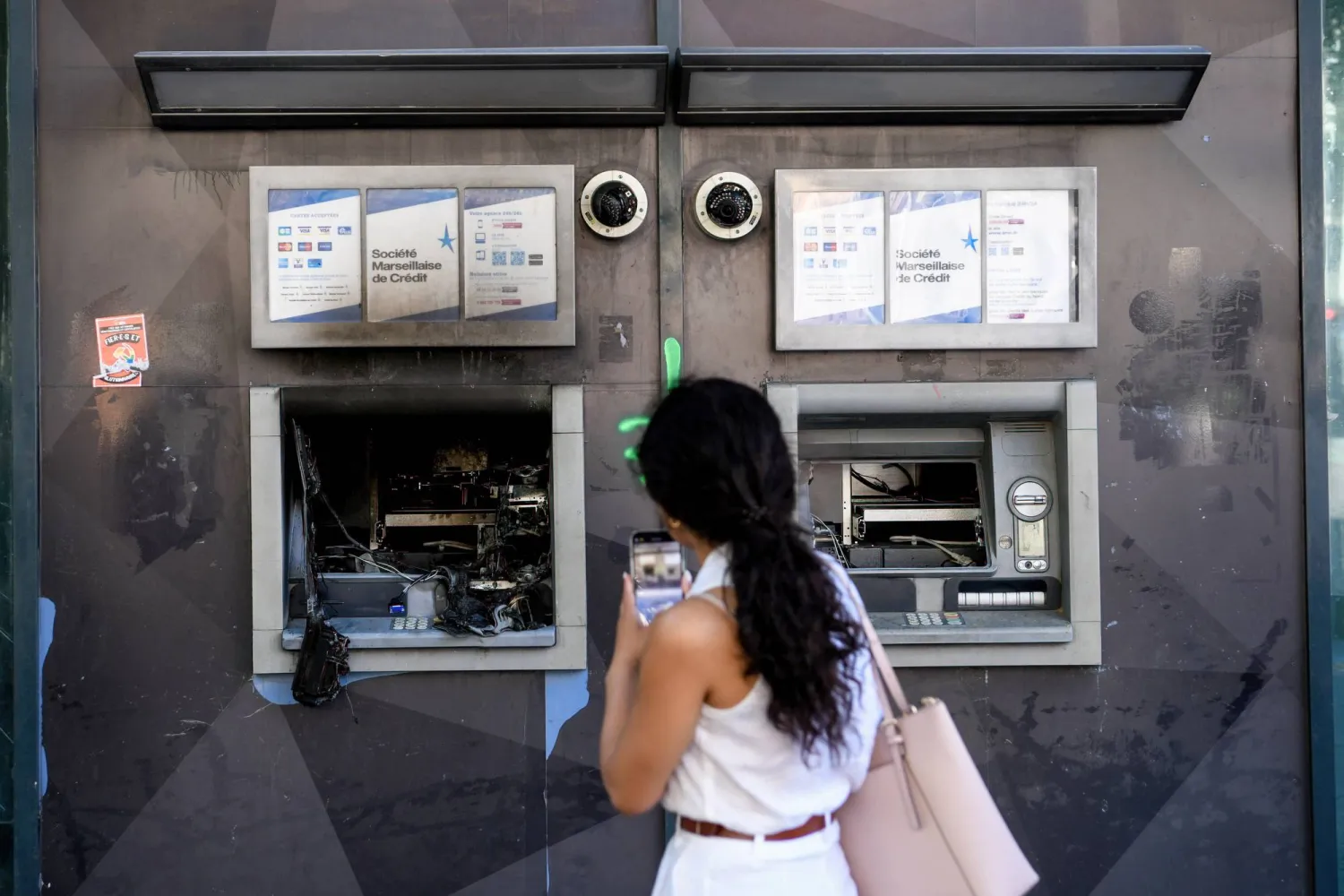 امرأة تصوّرصرافين آليين متضررين في مدينة مارسيليا (د.ب.أ)